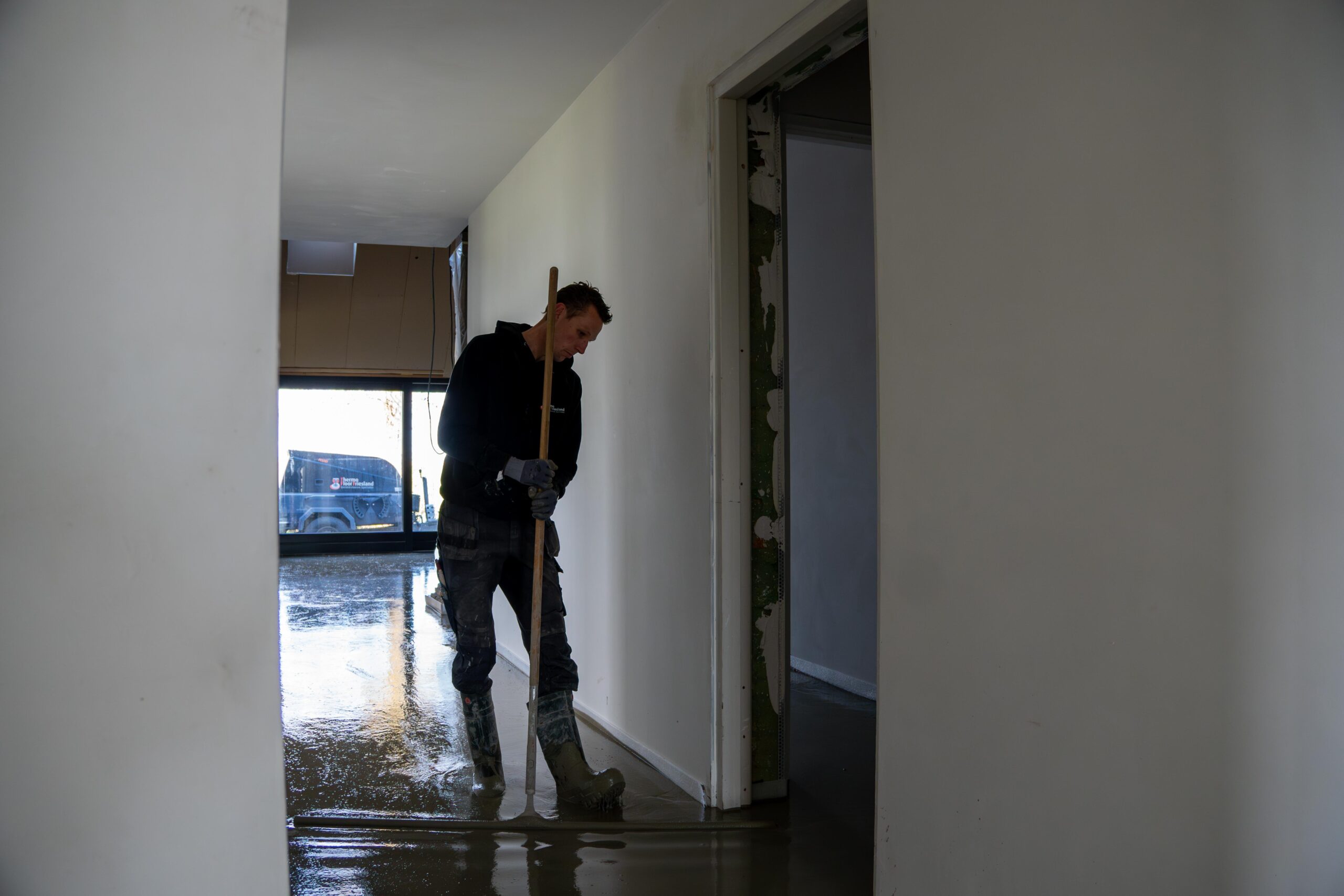 Een man veegt de vloer van een kamer met een bezem-thermo floor friesland(Oudega)