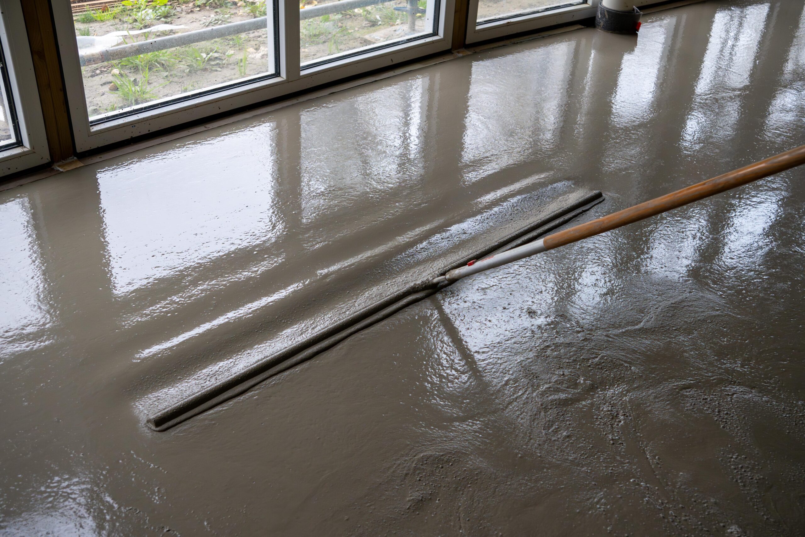 Een arbeider verspreidt cement over een vloer met een stok – Thermo Floor Friesland